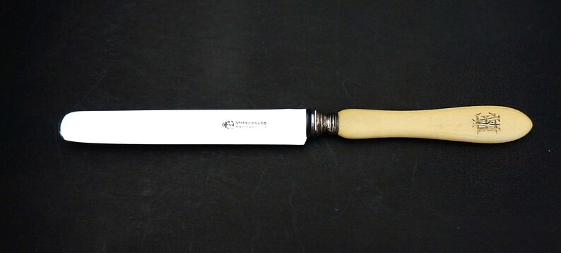 Puede incluir: Un cuchillo de mantequilla con mango blanco y hoja plateada. El mango es de hueso y tiene la inscripci&oacute;n "Shepherd  Sheffield".