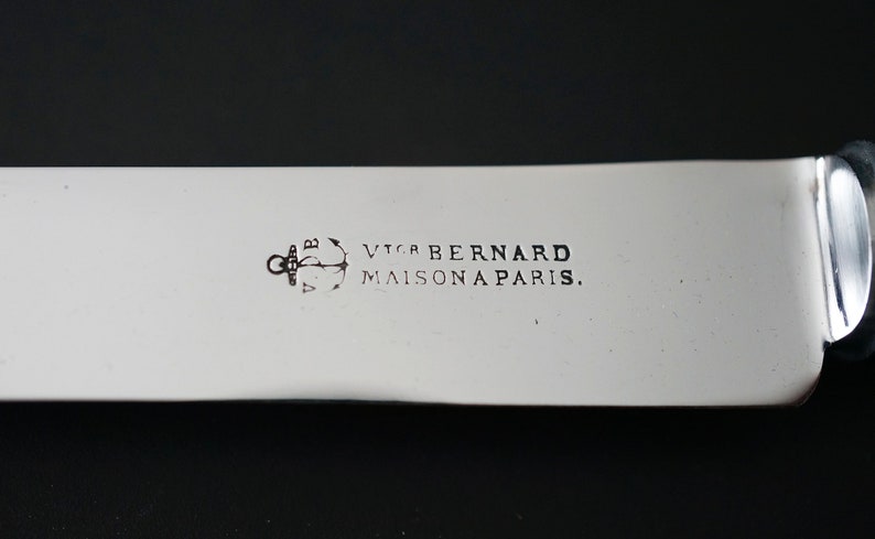 Puede incluir: Primer plano de un cuchillo de plata con mango negro. El cuchillo est&aacute; grabado con el texto "Victor Bernard Maison a Paris." y un ancla.