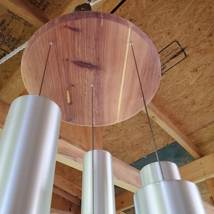May include: A wooden wind chime with a circular top and four silver tubes hanging from it. The wind chime is suspended from a ceiling.