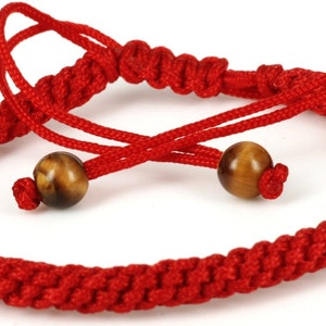 May include: Red braided string bracelet with two brown tiger eye beads.