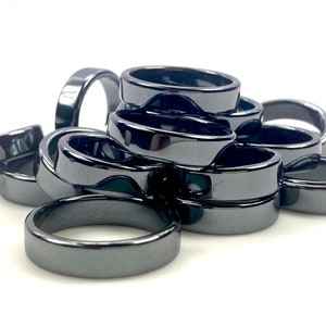 May include: A pile of black hematite rings, stacked and arranged in a loose, overlapping pattern. The rings are smooth and polished, with a slightly shiny finish.