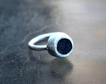 May include: A silver ring with a black circular inlay. The inlay has a textured surface.