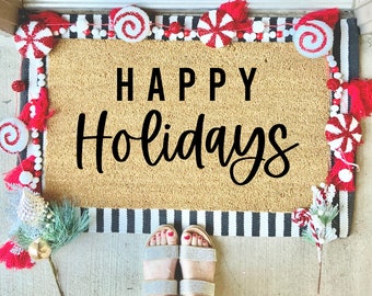 May include: A brown coir doormat with the text "HAPPY Holidays" in black lettering. The doormat is decorated with a white and red candy cane garland, red and white candy canes, and red and white pom-poms.