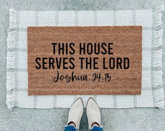 May include: A brown doormat with the text "This house serves the Lord Joshua 24:15" in black lettering.