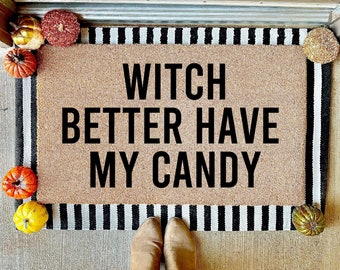 May include: A rectangular doormat with the text "WITCH BETTER HAVE MY CANDY" in black. The mat has a tan background with a black and white striped border. Decorative pumpkins in various colours surround the mat.