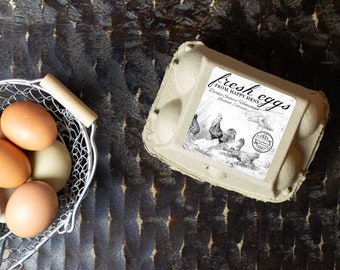 May include: A cardboard egg carton with a label that reads "fresh eggs from happy hens" and a drawing of chickens. The carton is sitting on a dark brown surface.