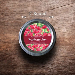 May include: A 2 inch round jar label with a red background and white text. The label says "PETERSON FAMILY Raspberry Jam" and "INGREDIENTS: SPECIFY YOUR NOTES OR INGREDIENTS HERE". The label has a watercolor illustration of raspberries and green leaves.