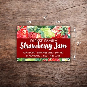 May include: A red and white label with a watercolor illustration of strawberries and green leaves. The label reads "DIRKSE FAMILY Strawberry Jam" and "CONTAINS: STRAWBERRIES, SUGAR, LEMON JUICE, PECTIN & LOVE".