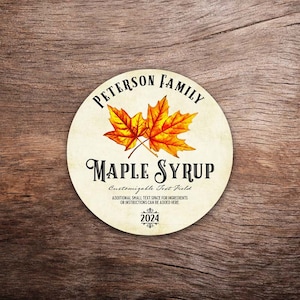May include: A round, cream-colored label with a brown woodgrain background. The label features a stylized black text that reads "Peterson Family Maple Syrup".  Two orange maple leaves are depicted in the center of the label.  The text "Customizable Text Field" is below the maple leaves.  The text "Additional small text space for ingredients or instructions can be added here" is below the "Customizable Text Field".  The year "2024" is at the bottom of the label.