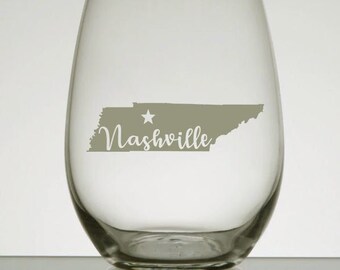 May include: A clear glass wine glass with a gray outline of the state of Tennessee and the word "Nashville" printed on it.