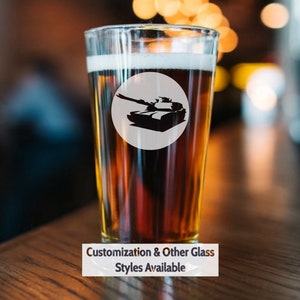 May include: A clear glass pint glass with a brown liquid inside. The glass has a white circle with a black silhouette of a tank on it. The text "Customization & Other Glass Styles Available" is below the glass.