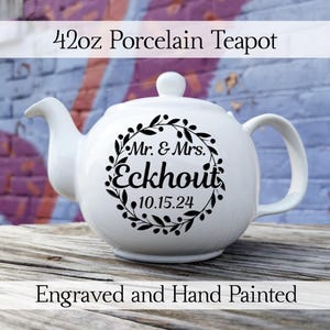 May include: White porcelain teapot with a black engraved design. The design features a wreath with leaves and berries, and the text "Mr. & Mrs. Eckhout 10.15.24". The teapot is 42 ounces.