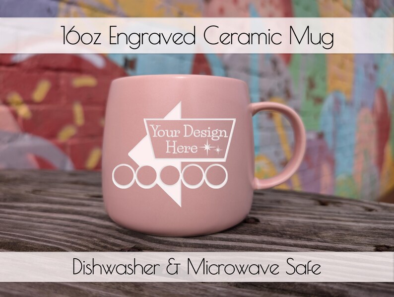 Op de afbeelding: Een roze 473ml gegraveerde keramische mok met een handvat. De mok heeft een wit ontwerp met de tekst "Your Design Here" en is gemarkeerd met "Dishwasher & Microwave Safe". De mok staat tegen een kleurrijke achtergrond.