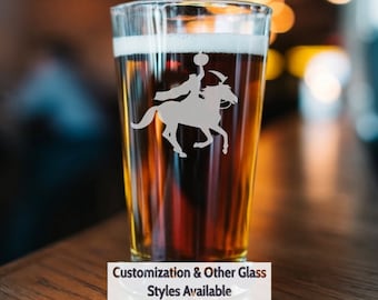 May include: A clear glass beer mug with a brown beer inside. The mug has a design of a person riding a horse with a pumpkin in their hand. The text "Customization & Other Glass Styles Available" is at the bottom of the image.
