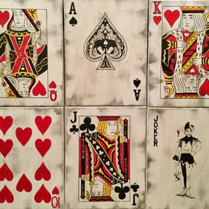 May include: A set of six painted playing cards, including the Queen of Hearts, Ace of Spades, King of Hearts, 10 of Hearts, Jack of Clubs, and a Joker. The cards are painted on a white background with a distressed, aged look.