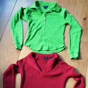 May include: Two long-sleeved shirts, one green and one red. The green shirt has a collar and button closure. The red shirt has a ribbed texture and a v-neck.