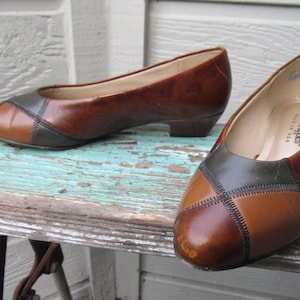 May include: A pair of brown leather shoes with a patchwork design in brown, tan, and dark green. The shoes have a low heel and are made in the USA.