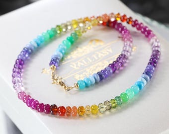 May include: A necklace composed of small, round, translucent beads arranged in a vibrant rainbow color gradient. The beads transition from red, orange, and yellow to green, blue, and purple. A gold-toned metal clasp secures the ends of the strand.