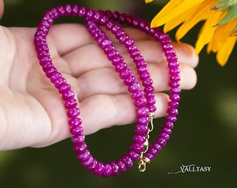 May include: A necklace composed of small, round, vibrant magenta beads with a polished finish. The strand features a gold-toned metal clasp mechanism at the end. The text VALLTASY is printed in the bottom right corner of the image.