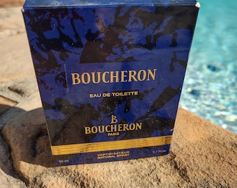 May include: A rectangular perfume box with the brand name "BOUCHERON" in gold lettering. The box is navy blue with a dark floral pattern and gold accents. The text "EAU DE TOILETTE" and "PARIS" are also visible.