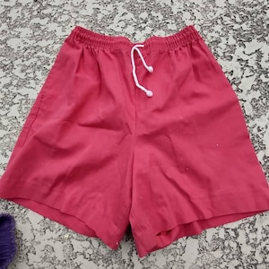 May include: Bright red shorts with an elasticated waistband and a white drawstring. The shorts are made of a smooth fabric and appear to be casual wear. The shorts are a solid colour and have a simple design.