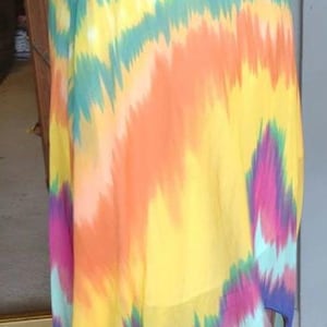 May include: A skirt featuring a wide, solid magenta waistband and a flowing, lightweight fabric with a vibrant, multi-coloured ikat-style pattern. The design includes vertical streaks of yellow, orange, teal, magenta, and deep blue colours.