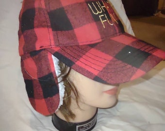 May include: Red and black plaid baseball cap with ear flaps. The cap has the embroidered text "Oh What Fun" in gold thread. The ear flaps are lined with white faux fur.