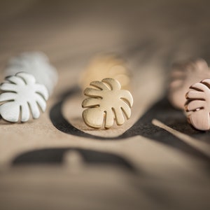 May include: Five gold, silver, and rose gold monstera leaf earrings. The earrings are small and delicate, and they are perfect for adding a touch of tropical style to any outfit.