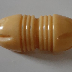 May include: A cream-colored, oval-shaped button with a ribbed design. The button has two small indentations on each side.