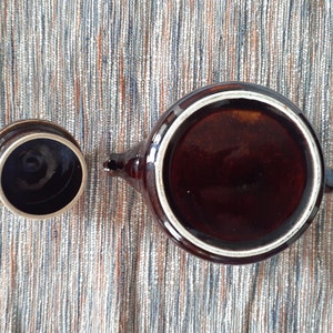 May include: A brown ceramic teapot with a white rim and a matching lid. The teapot is empty and the lid is off.