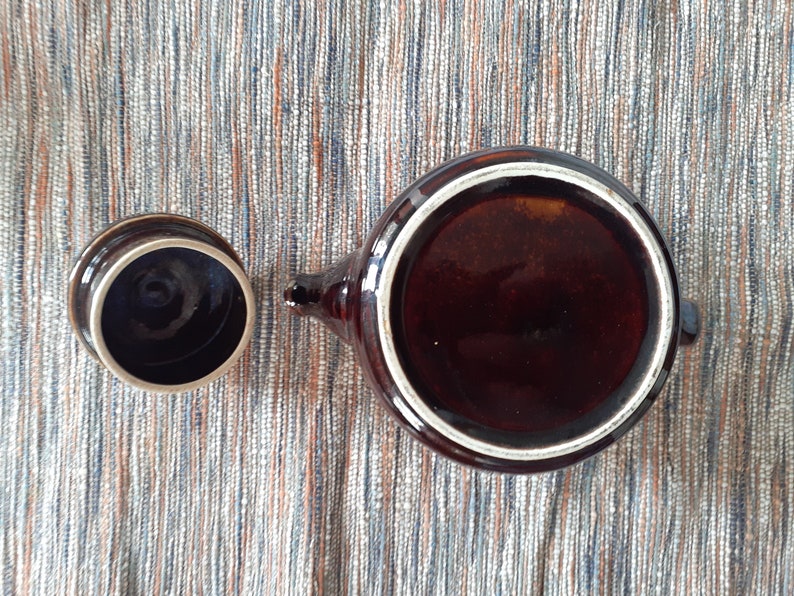 May include: A brown ceramic teapot with a white rim and a matching lid. The teapot is empty and the lid is off.