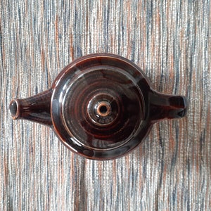 May include: A brown ceramic teapot with a round body and a single handle. The teapot has a small spout and a lid with a small hole in the center.