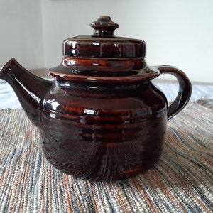 May include: A brown ceramic teapot with a lid and a handle. The teapot has a glossy finish and is decorated with a subtle pattern.