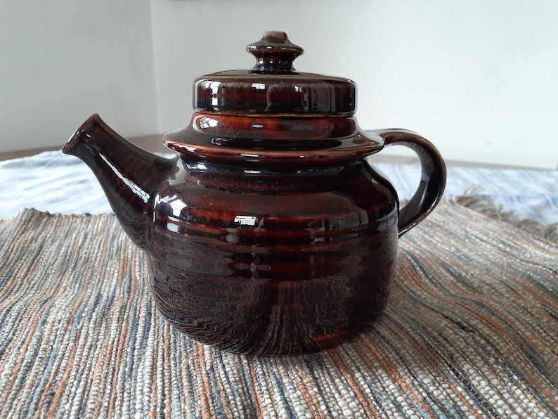 May include: A brown ceramic teapot with a lid and a handle. The teapot has a glossy finish and is decorated with a subtle pattern.