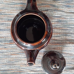 May include: A brown ceramic teapot with a lid. The teapot has a rounded body and a spout on the side. The lid is also brown and has a small knob on top.