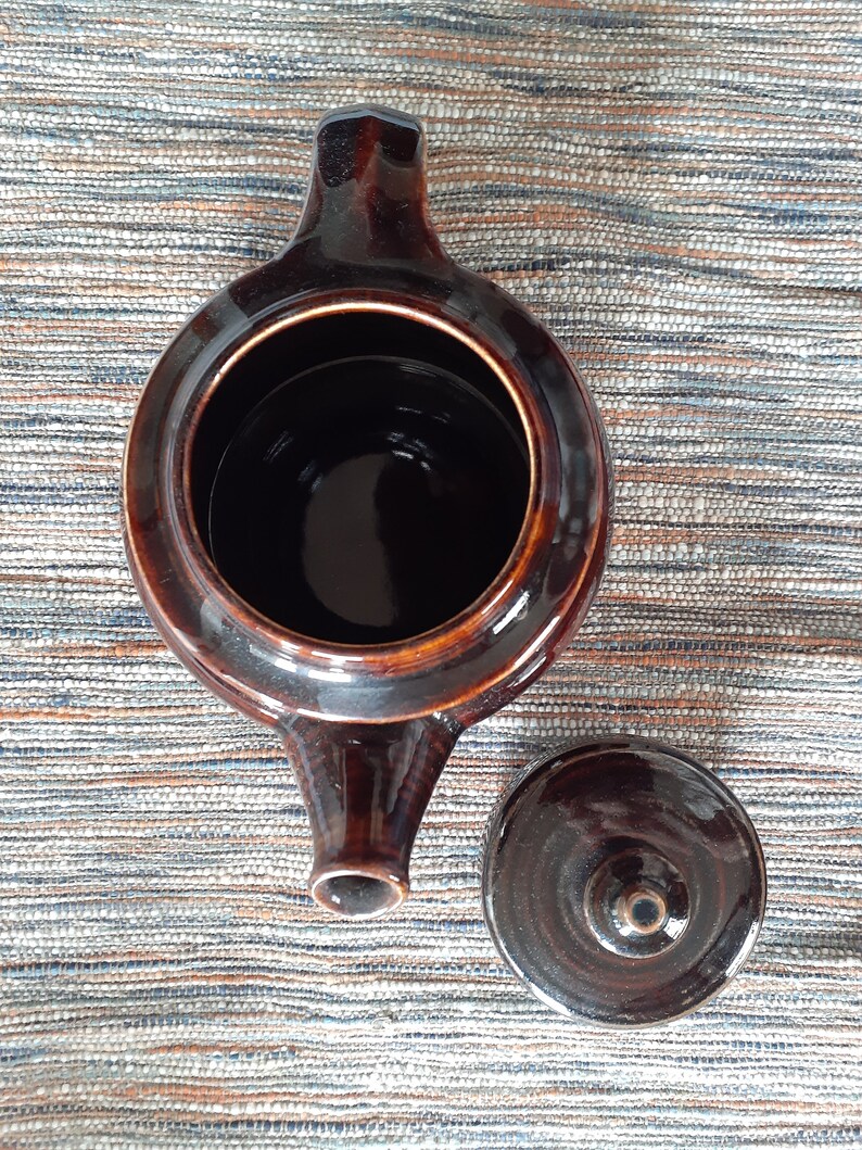 May include: A brown ceramic teapot with a lid. The teapot has a rounded body and a spout on the side. The lid is also brown and has a small knob on top.