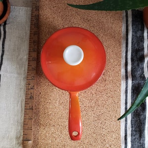 May include: Orange enameled cast iron saucepan with a white knob on the lid and a long orange handle.