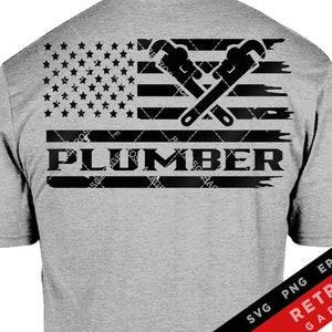 May include: A gray t-shirt with a black and white American flag design featuring crossed wrenches and the word "PLUMBER".