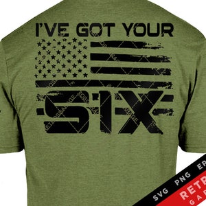 Può includere: Una maglietta verde con un designo di bandiera americana usurato e il testo "I've Got Your Six" in nero. Il testo è sovrapposto al designo della bandiera.