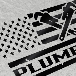 May include: A black and white graphic design of a wrench and pipe wrench crossed over a stylized American flag with the word "PLUMBER" below.