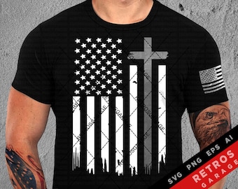 May include: A black t-shirt with a distressed white and gray American flag design featuring a cross. The flag is outlined in black and has a distressed look. The cross is also outlined in black and has a distressed look. The t-shirt has a crew neck and short sleeves.