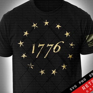 Pode incluir: Uma camiseta preta com um círculo dourado de estrelas e o número 1776 no centro. A camiseta tem um visual desgastado e é perfeita para um visual patriótico.