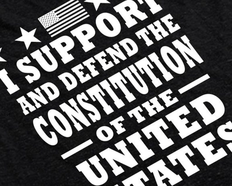 May include: Black t-shirt with white text that reads "I support and defend the Constitution of the United States". A small American flag is in the top left corner.