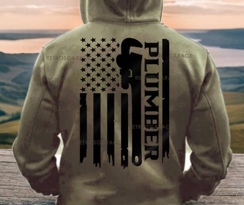 May include: A khaki hoodie featuring a distressed American flag design. The flag incorporates a wrench and the word "PLUMBER" in black. The hoodie has a hood and is viewed from the back.