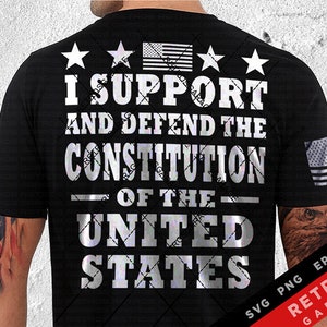 May include: A black t-shirt with a silver graphic that reads "I Support and Defend the Constitution of the United States". The graphic also includes four stars and an American flag. The t-shirt is being worn by a person with a tattoo of an eagle on their arm.