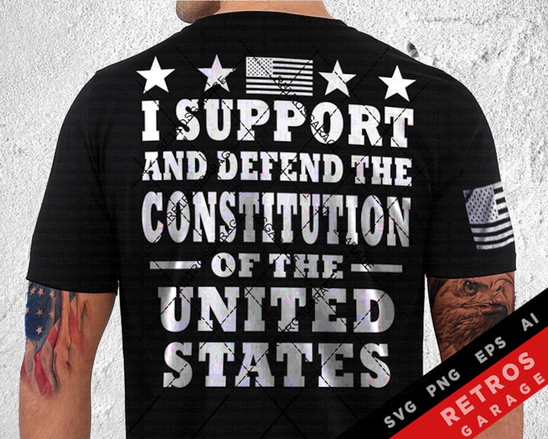 May include: A black t-shirt with a silver graphic that reads "I Support and Defend the Constitution of the United States". The graphic also includes four stars and an American flag. The t-shirt is being worn by a person with a tattoo of an eagle on their arm.