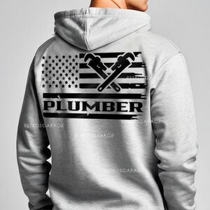 May include: A gray hooded sweatshirt with a black and white American flag design featuring two crossed wrenches and the word "PLUMBER" underneath.