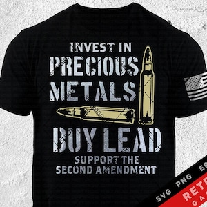 以下が含まれることがあります： 「貴重な金属に投資し、鉛を購入し、第二修正条項を支持しましょう」という、くたびれた白いグラフィックがプリントされた黒いTシャツ。グラフィックには、金色の弾丸が2つ描かれています。Tシャツの右袖には、小さなアメリカ国旗が付いています。