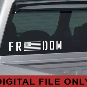 以下が含まれることがあります： 「FREEDOM」という文字とアメリカの旗のグラフィックが描かれた白いビニールステッカー。ステッカーはピックアップトラックのリアウィンドウに貼られています。