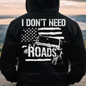 May include: Black hooded sweatshirt with a white graphic of a Jeep driving over an American flag with the text "I don't need roads".
